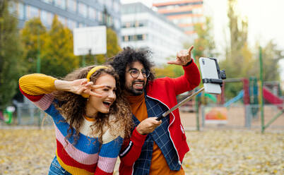 Porträt eines jungen Paares mit Smartphone, das im Freien im Park ein Video für soziale Medien aufnimmt. - HPIF16946