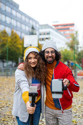 Porträt eines jungen Paares mit Smartphone, das im Freien im Park ein Video für soziale Medien aufnimmt. - HPIF16948