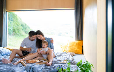 Junges Paar mit kleiner Tochter beim Frühstück im Haus, Wochenendausflug in einem Containerhaus auf dem Land. - HPIF16955