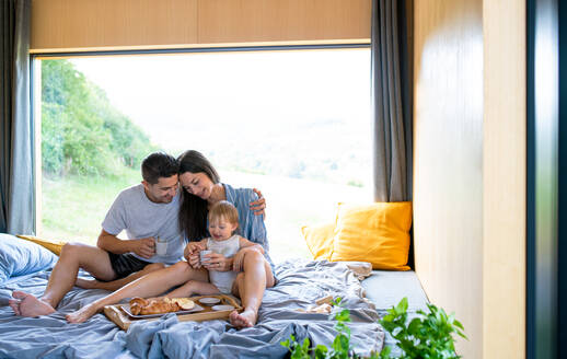 Junges Paar mit kleiner Tochter beim Frühstück im Haus, Wochenendausflug in einem Containerhaus auf dem Land. - HPIF16955
