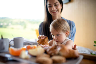Junge Frau mit kleiner Tochter beim Frühstück im Haus, Wochenendausflug in einem Containerhaus auf dem Lande. - HPIF16961