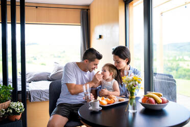 Junges Paar mit kleiner Tochter beim Frühstück im Haus, Wochenendausflug in einem Containerhaus auf dem Land. - HPIF16967