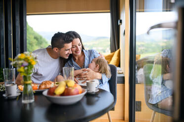 Junge Familie mit kleiner Tochter sitzt im Haus und verbringt das Wochenende in einem Containerhaus auf dem Land. - HPIF16968