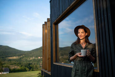 Young woman with coffee outdoors, weekend away in container house in countryside. - HPIF16976