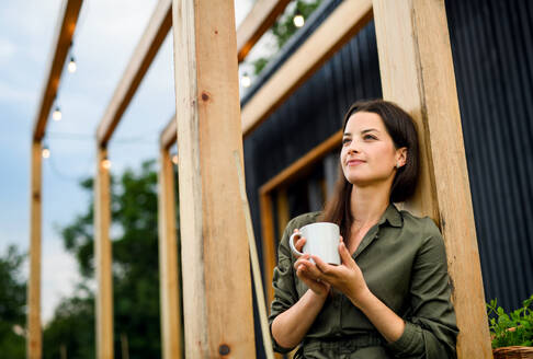 Young woman with coffee outdoors, weekend away in container house in countryside. - HPIF16991