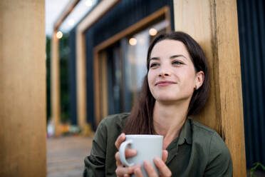 Portrait of young woman with coffee outdoors, weekend away in container house in countryside. - HPIF16992
