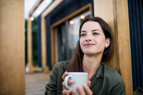 Porträt einer jungen Frau mit Kaffee im Freien, Wochenende in einem Containerhaus auf dem Lande. - HPIF16992