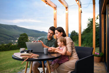 Junge Familie mit kleiner Tochter, die ihren Laptop im Freien benutzt, Wochenende in einem Containerhaus auf dem Lande. - HPIF16993