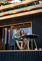 Junges Paar mit Laptop im Freien sitzend, Wochenendausflug im Containerhaus auf dem Lande. - HPIF16994