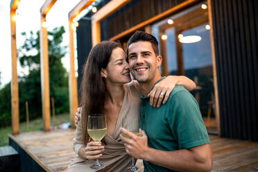 Young couple with wine sitting outdoors, weekend away in container house in countryside. - HPIF17000