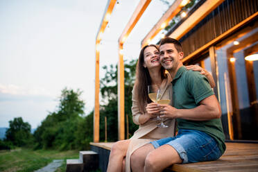 Young couple with wine sitting outdoors, weekend away in container house in countryside. - HPIF17001