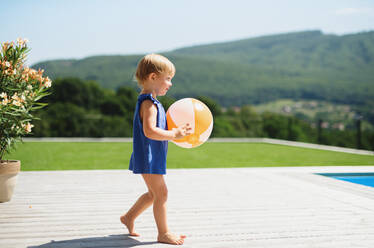 Side view portrait of small toddler girl with ball walking outdoors in backyard garden. - HPIF17014