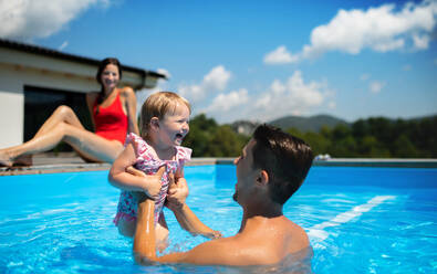 Fröhliche junge Familie mit kleiner Tochter im Swimmingpool im Garten, spielend. - HPIF17016