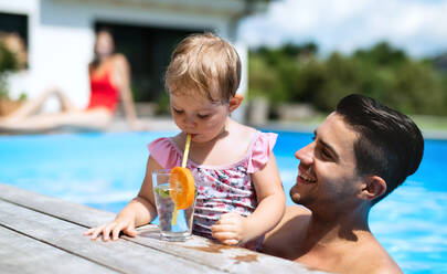 Portrait of small girl with father drinking lemonade in swimming pool outdoors in backyard garden. - HPIF17018