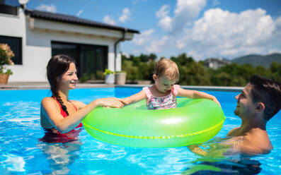 Happy young family with small daughter in swimming pool outdoors in backyard garden. - HPIF17020