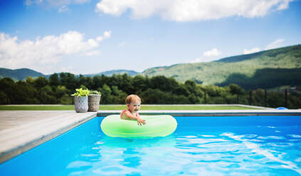 Portrait of small toddler girl with inflatable ring in swimming pool outdoors in backyard garden. - HPIF17024