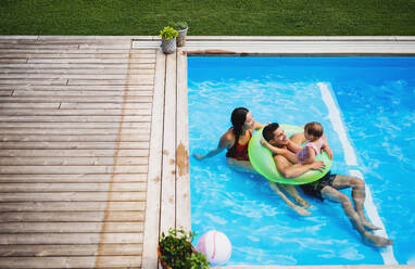 Draufsicht auf eine junge Familie mit einer kleinen Tochter im Swimmingpool im Hinterhofgarten. - HPIF17025