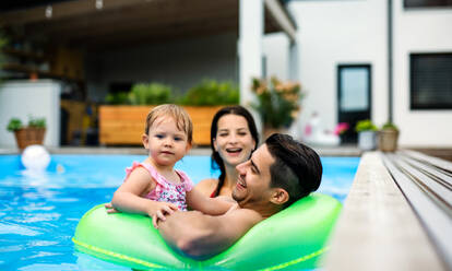 Happy young family with small daughter in swimming pool outdoors in backyard garden. - HPIF17026