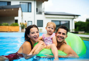 Glückliche junge Familie mit kleiner Tochter im Schwimmbad im Garten. - HPIF17029