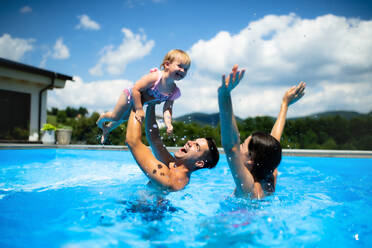 Fröhliche junge Familie mit kleiner Tochter im Swimmingpool im Garten, spielend. - HPIF17030