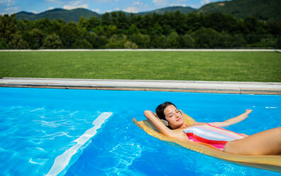 Young woman with headphones in swimming pool outdoors in backyard garden, relaxing. - HPIF17034