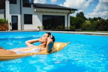 Young woman with headphones in swimming pool outdoors in backyard garden, relaxing. - HPIF17036