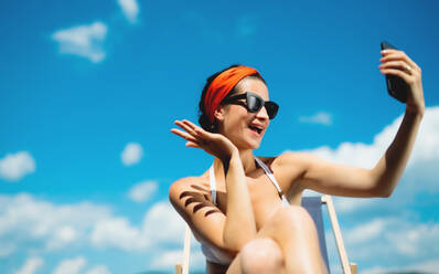 Eine junge Frau hält einen Moment der Entspannung am Pool fest und macht ein Selfie mit ihrem Smartphone - HPIF17037