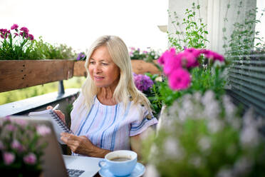 Aktive ältere Frau mit Laptop arbeitet auf dem Balkon, Home-Office-Konzept. - HPIF17138