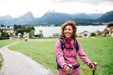 Eine ältere Frau mit Nordic-Walking-Stöcken wandert in der Natur und ruht sich aus. - HPIF17148