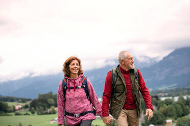 Frontansicht eines aktiven Rentnerpaares beim Wandern in der Natur, das sich an den Händen hält. - HPIF17167