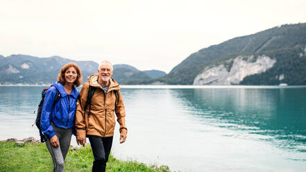 Ein älteres Rentnerpaar wandert an einem See in der Natur und hält sich an den Händen. copy space. - HPIF17207