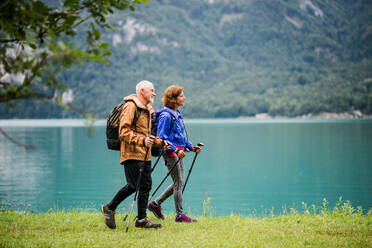 A side view of senior pensioner couple hiking by lake in nature, talking. Copy space. - HPIF17211