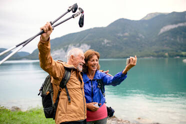 Ein glückliches älteres Paar fängt einen Moment in der Natur mit seinem Smartphone ein und posiert für ein Selfie am See - HPIF17217
