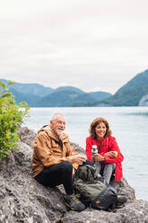 Ein fröhliches Rentnerpaar beim Wandern am See in der Natur, sitzend und ausruhend. - HPIF17219