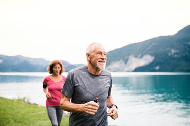 A senior pensioner couple with smartphone running by lake in nature. - HPIF17221