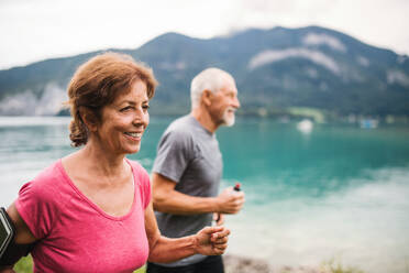 Ein älteres Rentnerpaar mit Smartphone läuft am See in der Natur. - HPIF17224