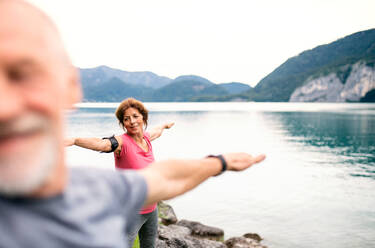 Ein älteres Rentnerehepaar beim Sport am See in der Natur, das sich dehnt. - HPIF17230