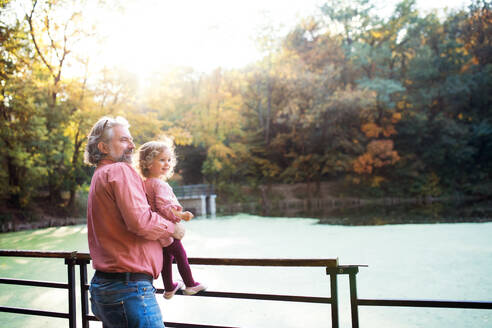 Reifer Vater mit Kleinkind Tochter stehen am See auf einem Spaziergang im Herbst Natur. - HPIF17249