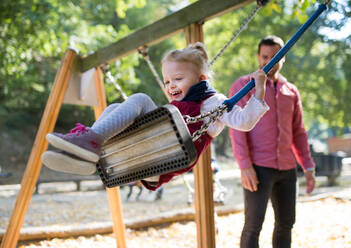 A cheerful small toddler girl with a father on a swing on a playground. - HPIF17279