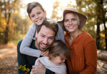 Eine schöne junge Familie mit kleinen Kindern bei einem Spaziergang im Herbstwald, die in die Kamera schaut. - HPIF17286