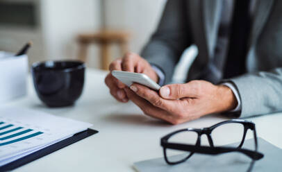 Ein Geschäftsmann mit Smartphone, Brille und Laptop, der am Tisch in einem Büro sitzt und arbeitet. Raum kopieren. - HPIF17333