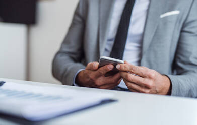 Ein Mittelteil eines Geschäftsmannes mit Smartphone und Laptop, der am Tisch in einem Büro sitzt und arbeitet. - HPIF17339