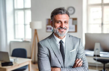 A cheerful mature businessman standing in an office, arms crossed. - HPIF17367