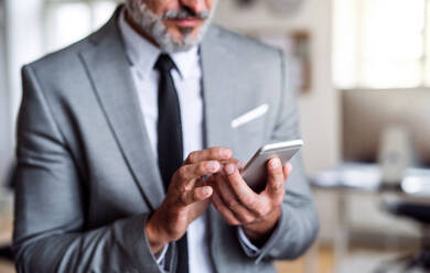 Ein unkenntlicher Geschäftsmann steht in einem Büro und benutzt ein Smartphone. - HPIF17368