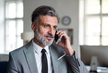 Ein seriöser reifer Geschäftsmann mit Smartphone in einem Büro, der einen Anruf tätigt. - HPIF17373