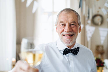 Porträt eines älteren Mannes, der in einem für eine Party eingerichteten Raum steht und ein Glas Wein in der Hand hält; Kopierraum. - HPIF17414