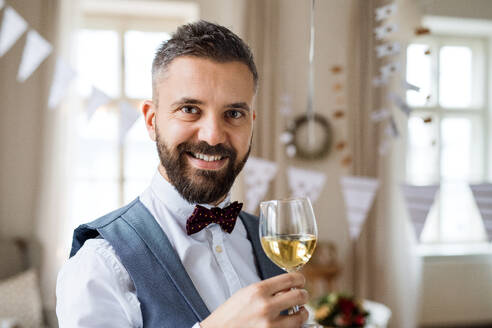 Porträt eines reifen Mannes, der in einem für eine Party eingerichteten Raum steht und ein Glas Wein in der Hand hält; Kopierraum. - HPIF17415