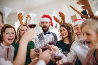 Eine Gruppe von Freunden mit Rentier-Stirnband und Weihnachtsmann-Hut stößt auf einer Indoor-Party mit Gläsern an. - HPIF17450