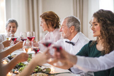 Eine große Familie sitzt an einem Tisch auf einer Indoor-Geburtstagsfeier und stößt mit Rotwein an. - HPIF17452