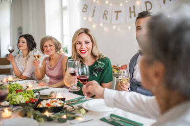 A big family sitting at a table on a indoor birthday party, clinking glasses with red wine. - HPIF17456